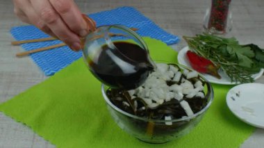 The cook is preparing a salad of kelp. Close-up female hand pouring brown seaweed salad with soy sauce from a clear gravy boat. The concept of healthy eating raw foods.