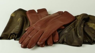 Zarif, kahverengi deri eldivenler yeşil bir eşarbın üzerinde, açık arkaplanda altın rengi bir renk var. Yeşil ve altın sarısı bir eşarpta, açık arkaplanda izole edilmiş bir çift yeni kahverengi deri eldiven..