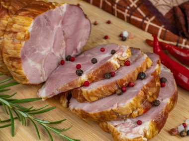 Sliced slices of juicy pork ham on a wooden cutting board, multi-colored allspice peas, red hot peppers and basil. Close-up. The concept of delicious meat products.
