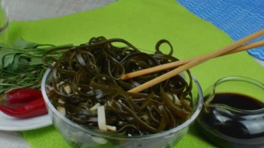 Seramik kasede yosun salatası ve ahşap yemek çubukları. Lezzetli yosun salatasıyla dönen kase, çeşitli otlarla dolu bir tabak ve kırmızı biber, soya soslu sos kasesi. Deniz ürünleri yemeği kavramı.