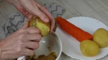 Removing the skin from boiled potatoes. A housewife with an iron kitchen knife peels a yellow-coloured potato into a plate and puts the peeled potatoes into a bowl. The concept of veganism. Close-up.