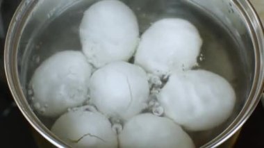 Iron pan with boiling water in which white chicken eggs are boiled. Water boils and boils in a pan with boiled chicken eggs. Process of cooking eggs on gas stove. Chef prepares eggs. Zoomed close-up.