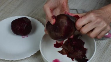 Cleaning boiled red beets. Close-up womans hand peels boiled red beets with a kitchen knife and puts the peeled beets in a plate. The concept of cooking boiled vegetables useful for health.