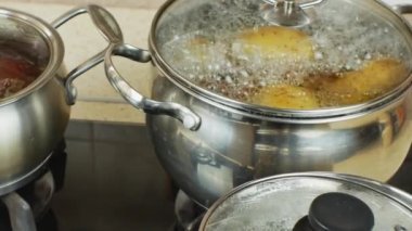 Potatoes, red beets and white chicken eggs are boiled in pots on a home gas stove. Potatoes, red beets and white chicken eggs boiled in boiling water in iron pans. Close-up. Zoomable focus.