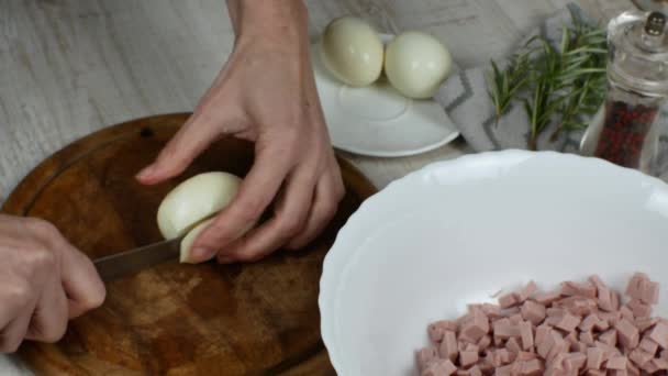 家庭主妇把煮熟的鸡蛋精细地切在木制切菜板上做肉色拉 用菜刀把煮熟的鸡蛋切在木板上的女性手的特写 — 图库视频影像