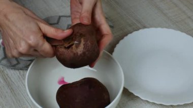 Kırmızı pancarların derisini yüzüyorum. Elinde demir mutfak bıçağı olan bir ev hanımı kırmızı pancarı bir tabağa soyar ve soyulmuş pancarı bir kaseye koyar. Veganlık kavramı. Yakın plan..