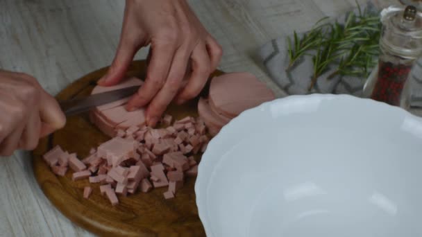 将香肠切割成圆圈 用刀在刨花板上切成小块 雌性手在灰色厨房桌子上的木制切菜板上用小刀细碎腊肠 肉类沙拉的烹调 — 图库视频影像