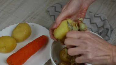 Peeling boiled potatoes. Womans hand close-up peels peel from a boiled yellow potato with kitchen knife and puts the peeled potatoes in plate. Concept of cooking boiled vegetables useful for health.