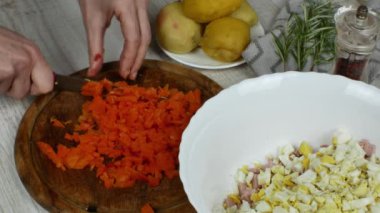 Housewife is chopping boiled carrots with kitchen knife on a wooden cutting board on a gray kitchen table. Close-up female hands chop boiled carrots for vegetable salad. The concept of vigaterianism.