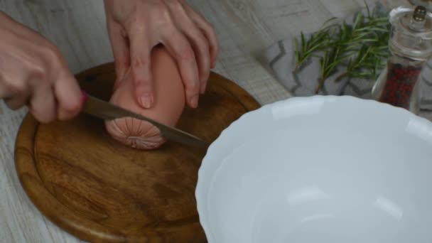 将煮熟的腊肠切成圆圈 用菜刀在木制切菜板上 用厨房铁刀在木制切菜板上切香肠 胡椒研磨机 迷迭香枝条 — 图库视频影像