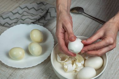 Removing the shell from boiled white eggs. A housewife takes an iron spoon and breaks the shell of a boiled chicken egg, peels the shell into a plate, puts the boiled egg into a bowl. Close-up.