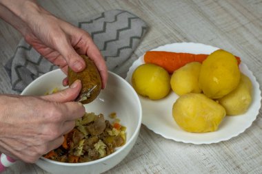 Peeling boiled potatoes. The female hand with an iron table knife removes the peel from the boiled yellow potatoes, puts the peeled potatoes on a plate. Close-up from the top side.
