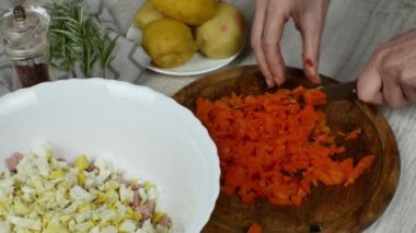 Haşlanmış havuçlar, ahşap kesim tahtasının üzerinde mutfak bıçağıyla doğranır, yanında sebze salatası, haşlanmış patatesli bir tabak, biber öğütücü, biberiye filizi.