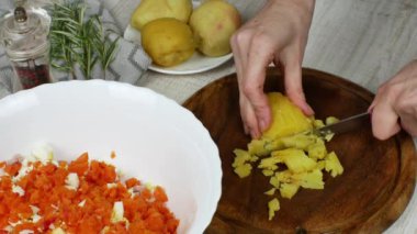 Kaynamış patatesler tahtanın üzerinde bıçakla küçük meydanlara ayrılır ve hazırlanmış et salatasıyla kaseye atılırlar. Yanında da haşlanmış patatesler, biber öğütücü, biberiye filizi bulunur..