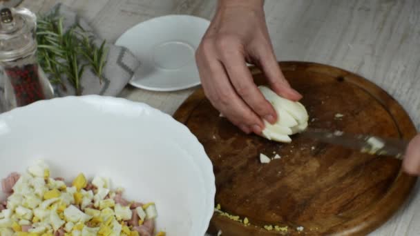 一位家庭主妇在一块木制的切菜板上精细地切下一只煮熟的鸡蛋 然后用刀把鸡蛋推进一个白色的玻璃碗里做肉沙拉 女性手部制作肉类沙拉的特写 — 图库视频影像