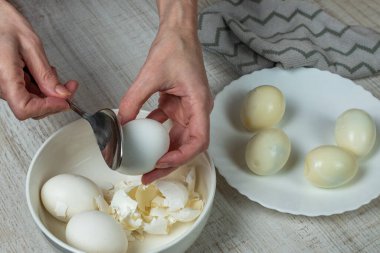 Haşlanmış beyaz yumurtaların kabuğunu çıkarıyorum. Bir ev hanımı demir kaşığı alır ve haşlanmış tavuk yumurtasının kabuğunu kırar, kabuğunu bir tabağa koyar, haşlanmış yumurtayı bir kaseye koyar. Yakın plan..