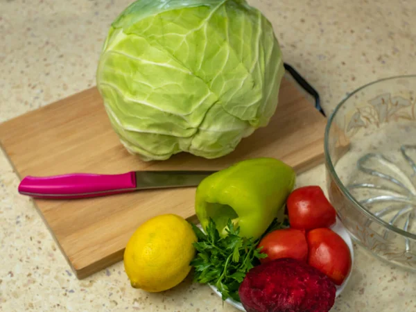 Tahta kesim tahtasında beyaz lahana, limon, kırmızı pancar, domates, dolmalık biber, mutfak masasında maydanoz. Taze sebzeli sağlıklı vegan salatası pişirmek. Çiğ sebze yeme kavramı.