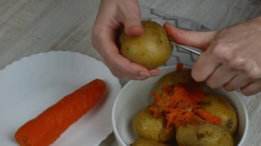 Peeling boiled potatoes. The female hand with an iron table knife removes the peel from the boiled yellow potatoes, puts the peeled potatoes on a plate. Close-up from the top side.