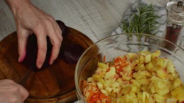 Kırmızı haşlanmış pancarlar, ahşap bir kesme tahtasının üzerinde mutfak bıçağıyla küçük parçalara ayrılır. Yanında bir kase et salatası, biber öğütücü, bir tutam biberiye bulunur..