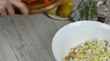 Ev hanımı, ahşap kesim tahtasının üzerinde mutfak bıçağıyla haşlanmış havuçları parçalıyor ve sebze salatası hazırlamak için havuçları kaseye koyuyor. Kadın elleri, yaklaşın. Vigaterianizm kavramı.