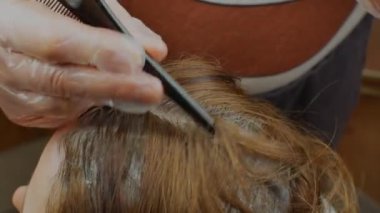 Kadın kuaför kadının saçını tarar ve boyar. Bir saç fırçasıyla müşterinin saçına kimyasal boya süren bir kuaför elinin yakın çekimi. Kadınların saç bakımı kavramı..