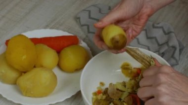 Peeling boiled potatoes. The female hand with an iron table knife removes the peel from the boiled yellow potatoes, puts the peeled potatoes on a plate. Close-up from the top side.