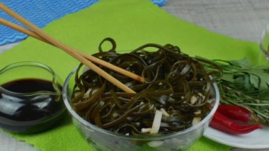 Seramik kasede yosun salatası ve ahşap yemek çubukları. Lezzetli yosun salatasıyla dönen kase, çeşitli otlarla dolu bir tabak ve kırmızı biber, soya soslu sos kasesi. Deniz ürünleri yemeği kavramı.