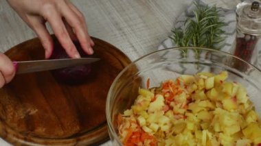 A housewife cuts red boiled beets with a kitchen knife on a wooden cutting board on a gray kitchen table. Close-up female hand cuts red boiled beets for vegetable salad. The concept of vigaterianism