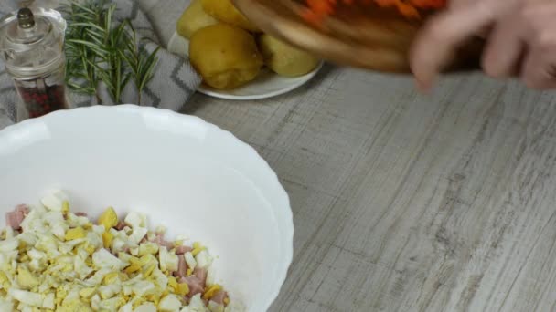 烤胡萝卜用菜刀在木制切菜板上切碎 然后倒入碗中 准备肉色拉 旁边是平底锅和煮熟的土豆 胡椒研磨机 迷迭香 — 图库视频影像