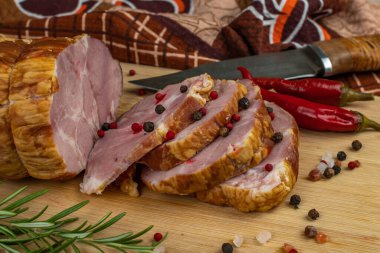 Slices of juicy and delicious pork bacon on a wooden cutting board with a carving knife, multi-colored allspice peas, red hot peppers, parsley, dill and basil. The concept of meat products.