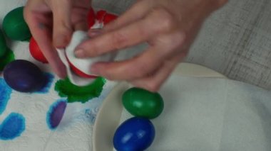 Çok renkli boyanmış Paskalya yumurtalarını sebze yağıyla ovuşturan kadın elleri. Yumurtaları parlatmak için çok renkli Paskalya yumurtalarını sebze yağıyla ovuyorum. Mutlu Paskalyalar. Paskalya kutlaması.