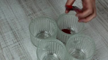 Ev hanımı Paskalya tavuğu yumurtalarını boyamak için gıda boyası üretiyor. Paskalya tavuğu yumurtalarını farklı renklerde boyamak için cam bardaklara besin döken kadın elinin yakın çekimi. Paskalya tatili konsepti.