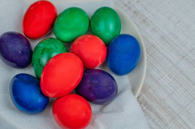 Farklı renklerde boyanmış renkli Paskalya tavuğu yumurtaları mutfak masasındaki beyaz bir tabakta yatıyor. Paskalya bayramı ve boyalı Paskalya yumurtaları kavramı. Hıristiyan inancıyla Paskalya. 