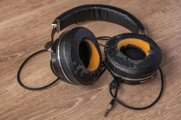 Eski siyah kulaklıklar, açık ahşap bir masaya yakın plan. Yüksek kalitede müzik dinle. Elektronik cihazların düzenli olarak değiştirilmesi gerekiyor. Kaliteli müzik dinleme için elektronik aygıtlar kavramı.