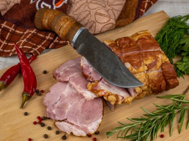 Tahta bir kesme tahtasında, dilimlenmiş domuz jambonu, et bıçağı, kırmızı acı biber, çok renkli baharat, maydanoz, dereotu ve fesleğen. Lezzetli domuz ürünleri konsepti.