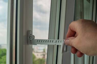 Usta plastik bir pencere açmak ve işlevini kontrol etmek için sınırlayıcı yükledi. Pencere ayarlarını kontrol eden bir elin yakın çekimi. Ev tamiri. Pencere donanımı kuruluyor.