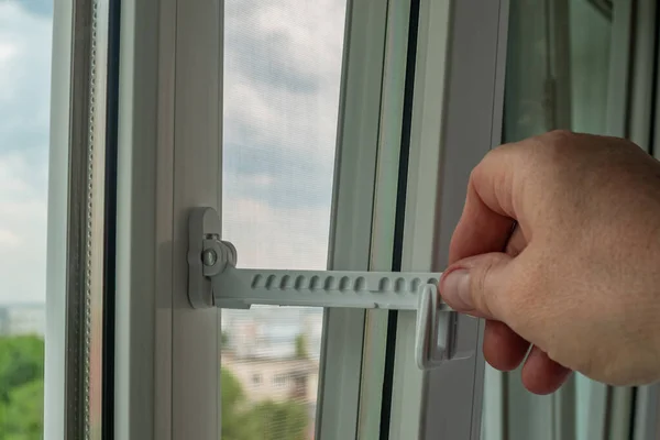 Master installed fixing limiter for opening a plastic window and checks its operation. Close-up of a hand checking the operation of window fittings. Home repairs. Installing window hardware.