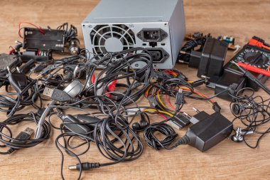 Eski kablolar, bağlantılar, kulaklıklar ve şarj aletleri ahşap bir masanın üzerine yığılmış. Eski elementlerin ve elektronik cihazların parçalarının değiştirilmesi. Bozuk elektronik cihazların ve elementlerinin onarımı.