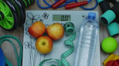 Üzerinde elmalar olan zemin pulları, su şişeleri, mezura, halterler, halterler, spor bantları, top, akupunktur topları, ip atlama. Fitness ayarlandı. Aşırı kilolu ve obezite kavramı.