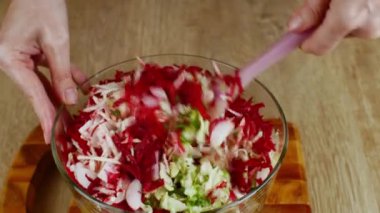 Kadın eli, cam salata kasesinde doğranmış sebzeleri silikon spatulayla karıştırıyor. Taze sebze salatası hazırlıyorum. Sağlıklı beslenme kavramı bir yaşam tarzı olarak.