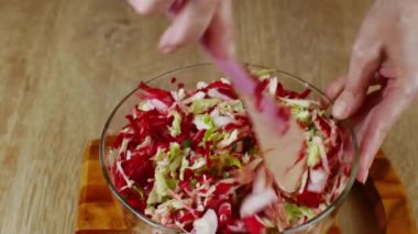 Ev hanımı cam kasede plastik spatulayla taze sebze salatası karıştırıyor. Cam salata kasesinde plastik kaşıkla salata karıştıran bir kadının yakın çekimi. Vejetaryenlik ve çiğ gıda kavramı.