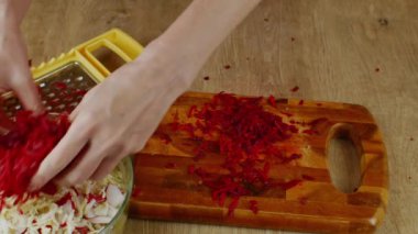 Bir ev hanımı demir rendesine kırmızı pancar sürer. Sebze salatası için sebze rendesine kırmızı pancar süren kadın ellerinin yakın çekimi. Vejetaryenlik ve çiğ gıda kavramı..