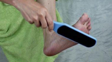 Dişi, ayağını temizlemek için bir zımpara fırçası kullanıyor. Kadınlarda çatlak topukluların tedavisi. Bir kadın topukluların derisi için plastik rendeleyiciyle kozmetik işlemler yapar. Nasır temizleme kavramı.