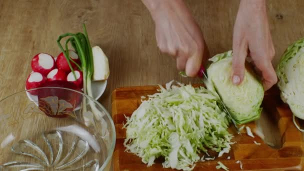 木製のまな板に新鮮な白菜を切るために女性はキッチンナイフを使用しています 夏のサラダを作るためにキャベツを切り刻むクローズアップ女性の手 家庭のキッチンで料理を作るというコンセプト — ストック動画