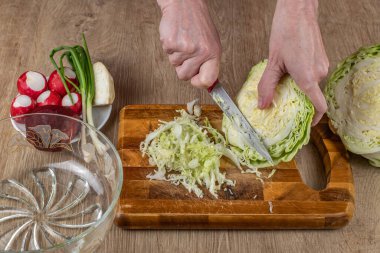 Bir kadın ahşap kesme tahtasındaki taze beyaz lahana kesmek için mutfak bıçağı kullanıyor. Yaz salatası yapmak için lahana doğrayan kadın elleri. Ev mutfağında yemek pişirme kavramı..