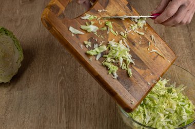 Kadının biri bıçakla doğranmış lahanayı bir kase salataya sokuyor. Bir ev hanımı taze sebze salatası hazırlar. Taze sebzelerden salata pişirme kavramı