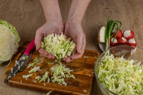 stock image The woman takes shredded white cabbage with her hands and puts the cabbage in a bowl of salad. A housewife prepares a salad of fresh vegetables. The concept of cooking salads from fresh vegetables.