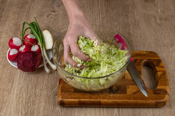 stock image Close-up of a woman's hand salting and stirring shredded white cabbage in a salad bowl. Preparing fresh vegan vegetable salad. The concept of veganism and raw food are good for health.