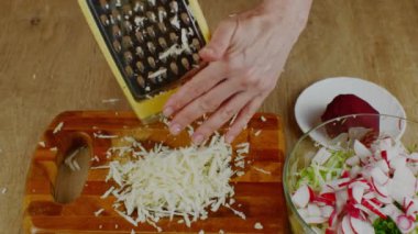 Bir ev hanımı demir rendesine kereviz kökü sürer. Sebze salatası için sebze rendesinin üzerine kereviz kökü süren kadın ellerine yakın plan. Vejetaryenlik ve çiğ gıda kavramı..