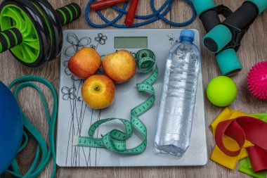 Üzerinde elmalar olan zemin pulları, su şişeleri, mezura, halterler, halterler, spor bantları, top, akupunktur topları, ip atlama. Fitness ayarlandı. Aşırı kilolu ve obezite kavramı.